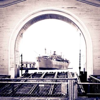 Looking down a dock through an arched brick work to a ship.